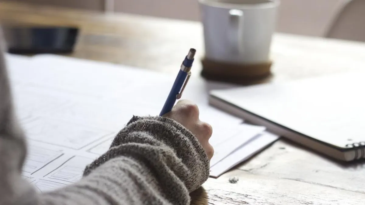 A writer's notebook and pen on a wooden desk beside a laptop