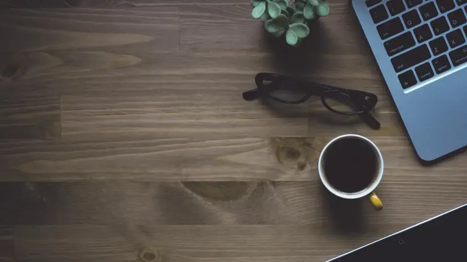 A laptop, glasses and coffee on a wooden desk seen from above